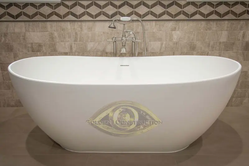 A white freestanding tub with a floor-standing filler in front of stone wall tile with a geometric border