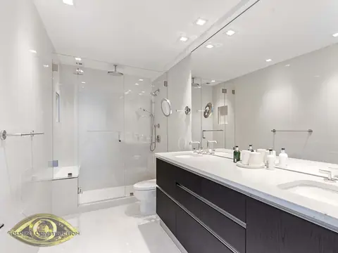 A white bathroom with a long dark double vanity under a white top, a wall-width mirror and a frameless glass shower