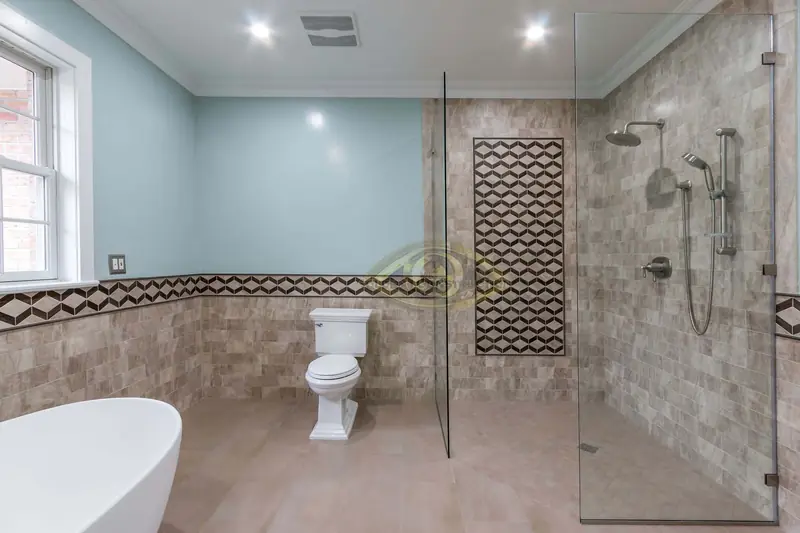 A bathroom with pale blue walls, stone wall tile under a geometric border, a glass walk-in shower with a mosaic panel and a toilet