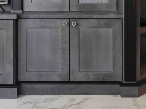 Panelled doors with ring pulls at the base of a grey stained built-in, above a black baseboard on a marble floor