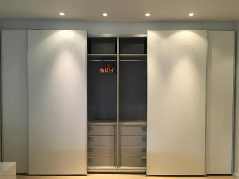 A closet with white sliding doors open on a lit interior with drawers, shelves and a hanging rail