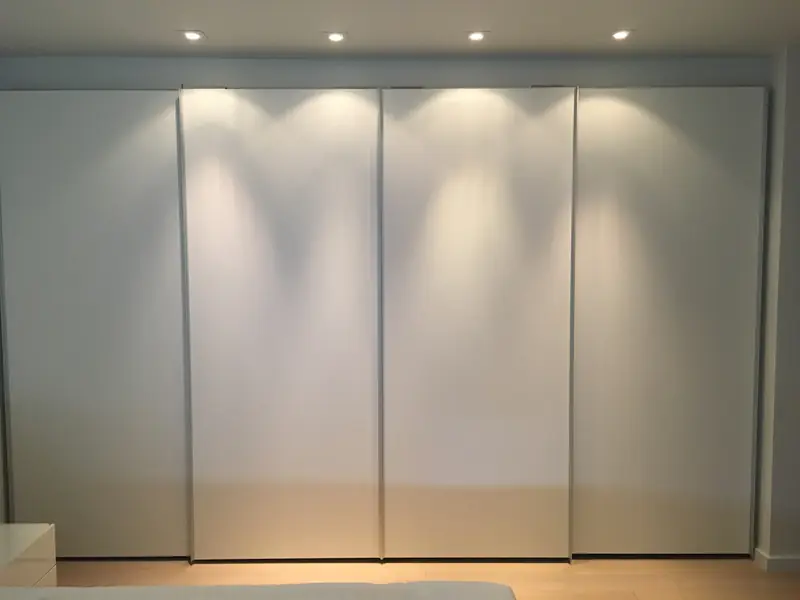 A wall of four tall white sliding closet doors lit from the ceiling