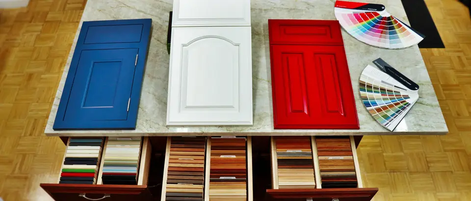 Cabinet door samples in blue, white and red on a stone slab, with paint colour fans and drawers of wood and laminate samples