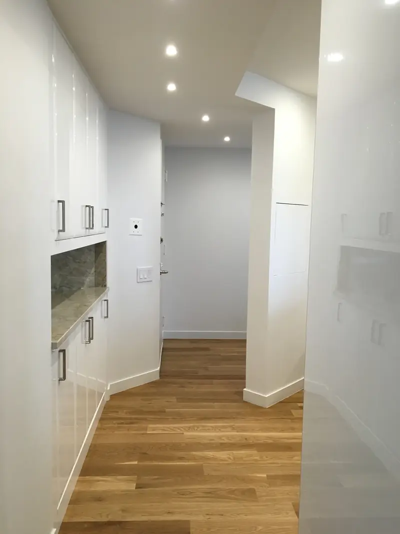 A hallway lined with a white lacquer storage wall with a stone niche, on an oak floor