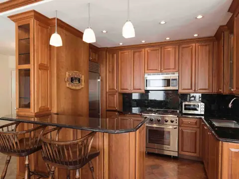 A kitchen with cherry raised-panel cabinets, black granite counters, a peninsula bar with two wooden stools and three pendant lights