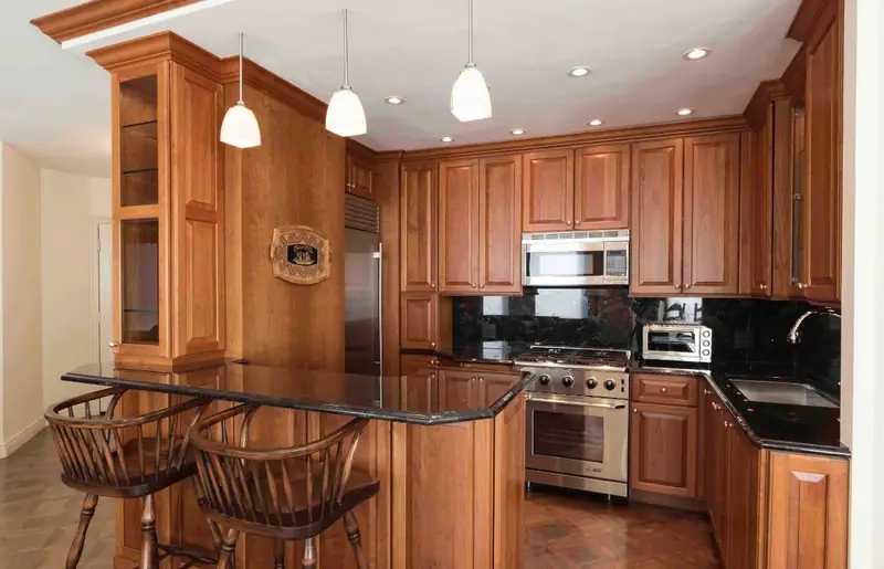 A kitchen with cherry raised-panel cabinets, black granite counters, a peninsula bar with two wooden stools and three pendant lights
