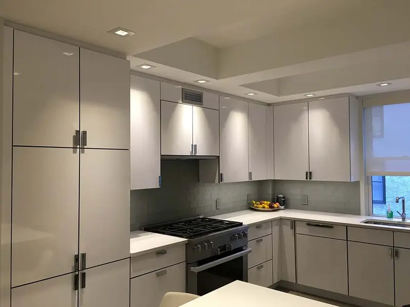 A kitchen with grey lacquer cabinets from floor to ceiling, a panelled refrigerator, a range and a recessed ceiling