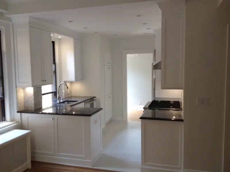 A kitchen with white panelled cabinets and black stone counters, with a sink under a window