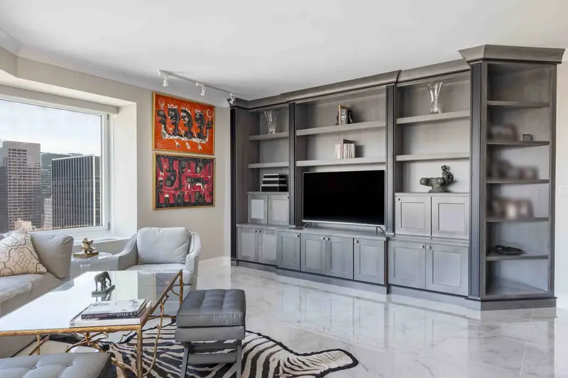 A living room with a grey stained built-in media wall around a television, a white marble floor and a zebra hide rug
