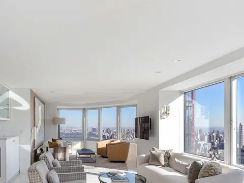 A white living room with windows onto a skyline, a sofa and armchairs around a glass table and white built-in cabinets