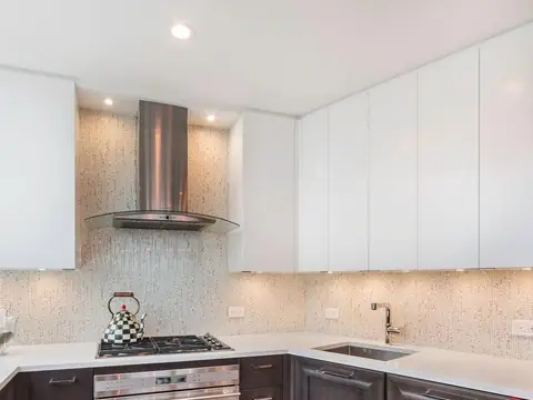 A kitchen corner with white wall cabinets, a steel and glass hood over a gas cooktop and a mosaic backsplash